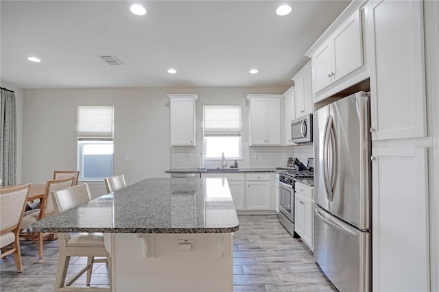 kitchen featuring a breakfast bar, dark stone counters, appliances with stainless steel finishes, a kitchen island, and white cabinetry