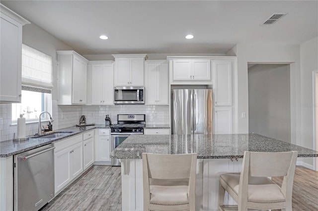 kitchen with appliances with stainless steel finishes, dark stone counters, sink, white cabinets, and a kitchen island