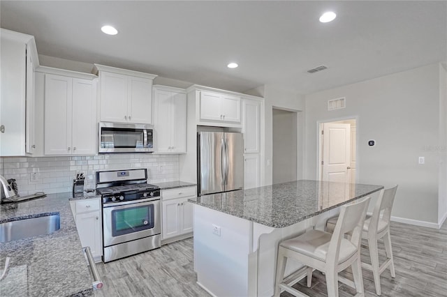 kitchen with sink, light stone countertops, a kitchen island, white cabinetry, and stainless steel appliances