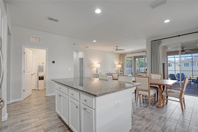 kitchen featuring ceiling fan, a center island, white cabinetry, and dark stone counters