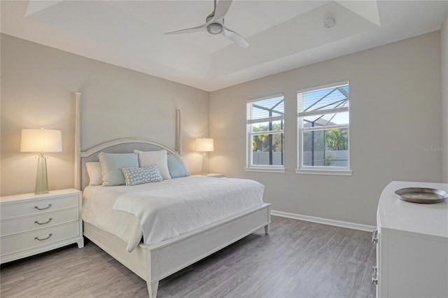 bedroom with ceiling fan, light hardwood / wood-style floors, and a raised ceiling