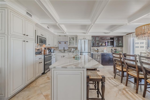 kitchen featuring light stone countertops, white cabinetry, a kitchen bar, a kitchen island, and appliances with stainless steel finishes