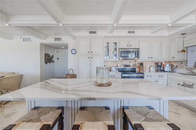 kitchen with light stone countertops, hanging light fixtures, tasteful backsplash, a breakfast bar, and appliances with stainless steel finishes