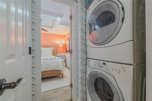 clothes washing area featuring light hardwood / wood-style floors, stacked washer and clothes dryer, and ornamental molding