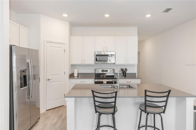 kitchen with a kitchen island with sink, white cabinets, stainless steel appliances, and light hardwood / wood-style floors