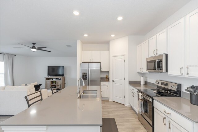 kitchen featuring appliances with stainless steel finishes, ceiling fan, sink, white cabinetry, and an island with sink