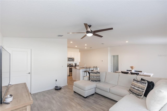 living room featuring ceiling fan, light hardwood / wood-style floors, and a textured ceiling