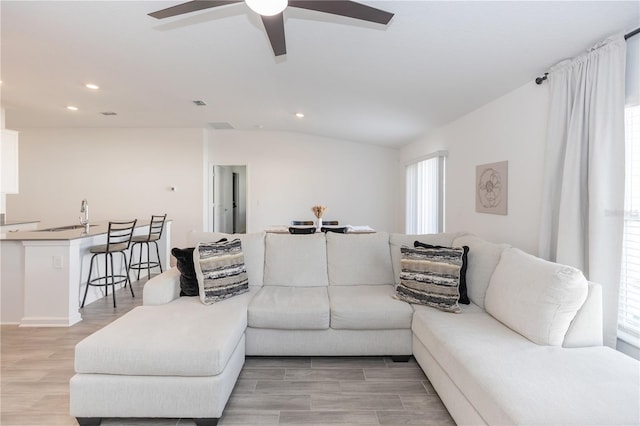 living room with ceiling fan, vaulted ceiling, sink, and light hardwood / wood-style flooring