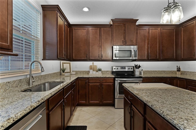 kitchen featuring light stone counters, stainless steel appliances, sink, pendant lighting, and light tile patterned flooring