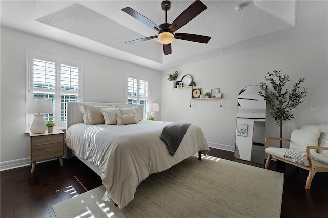 bedroom featuring ceiling fan, dark hardwood / wood-style flooring, a textured ceiling, and a tray ceiling