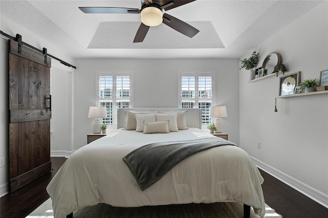 bedroom featuring a textured ceiling, a tray ceiling, ceiling fan, a barn door, and hardwood / wood-style floors