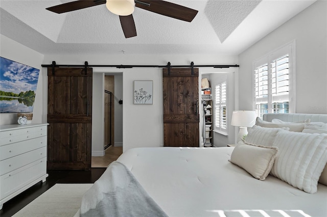 bedroom featuring ceiling fan, a barn door, dark wood-type flooring, and a textured ceiling