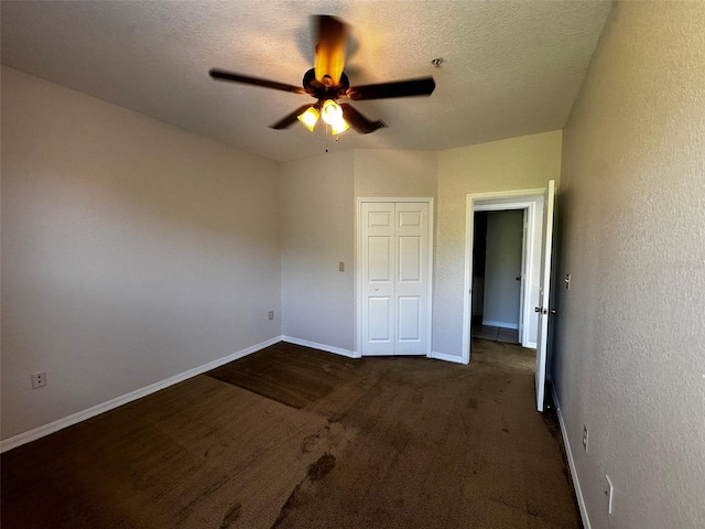 unfurnished bedroom featuring ceiling fan, a textured ceiling, a closet, and dark colored carpet