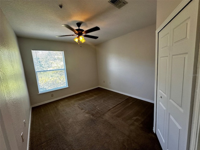 unfurnished bedroom featuring a textured ceiling, ceiling fan, a closet, and dark colored carpet