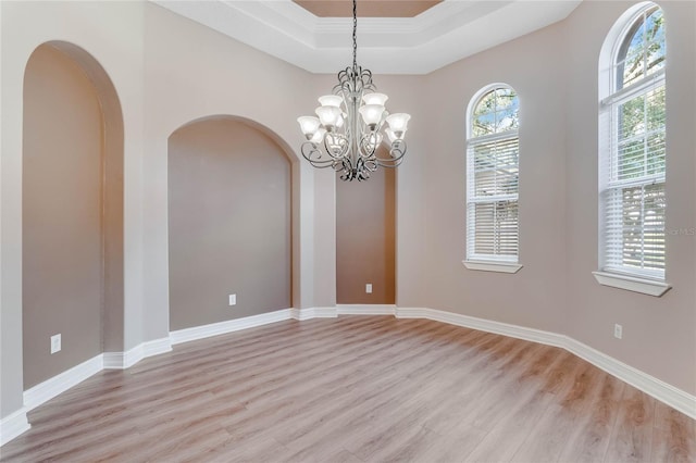 empty room featuring a notable chandelier, light hardwood / wood-style floors, a raised ceiling, and crown molding