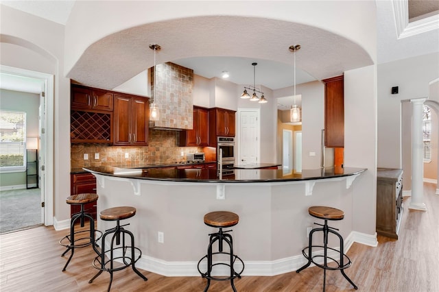 kitchen featuring pendant lighting, a kitchen breakfast bar, kitchen peninsula, and decorative columns