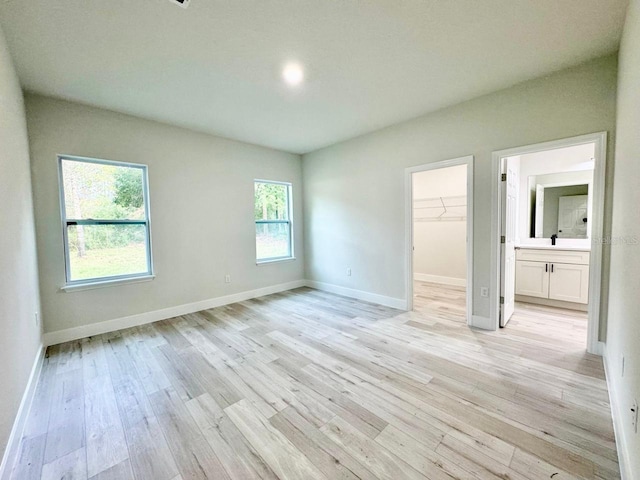 unfurnished bedroom with a walk in closet, light wood-type flooring, connected bathroom, and multiple windows