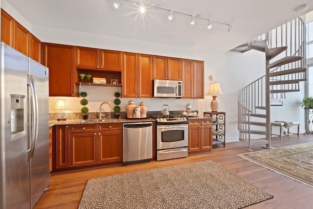 kitchen featuring sink, stainless steel appliances, track lighting, light stone countertops, and light wood-type flooring