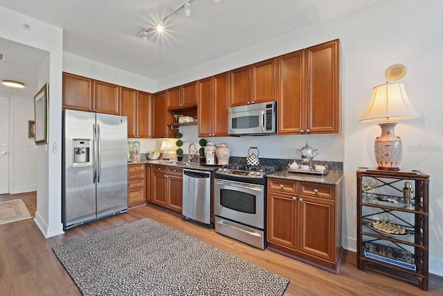 kitchen with sink, wood-type flooring, dark stone countertops, track lighting, and stainless steel appliances