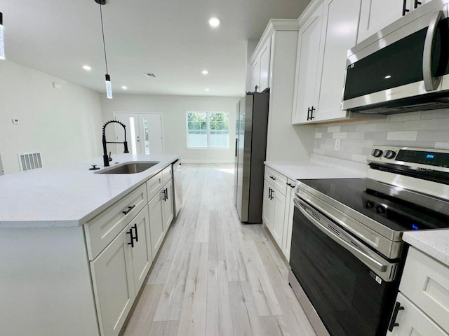 kitchen with sink, stainless steel appliances, pendant lighting, light hardwood / wood-style floors, and white cabinets