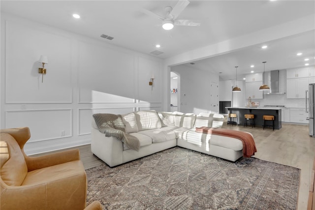 living room with light hardwood / wood-style floors, ceiling fan, and sink