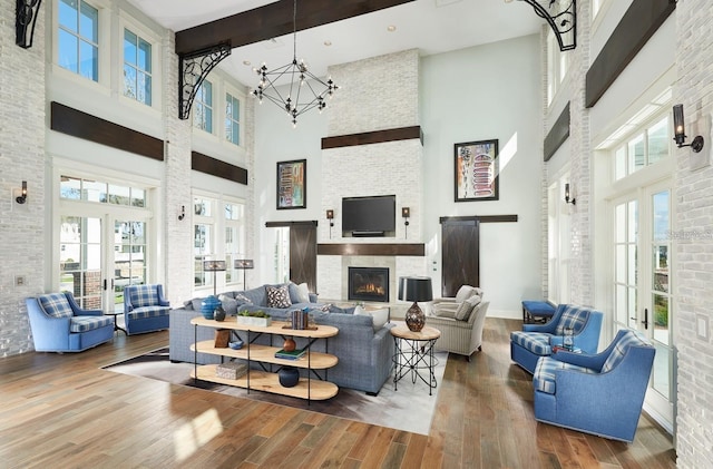 living room featuring french doors, a towering ceiling, a notable chandelier, hardwood / wood-style floors, and a stone fireplace