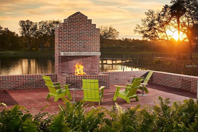 patio terrace at dusk with a water view and an outdoor brick fireplace