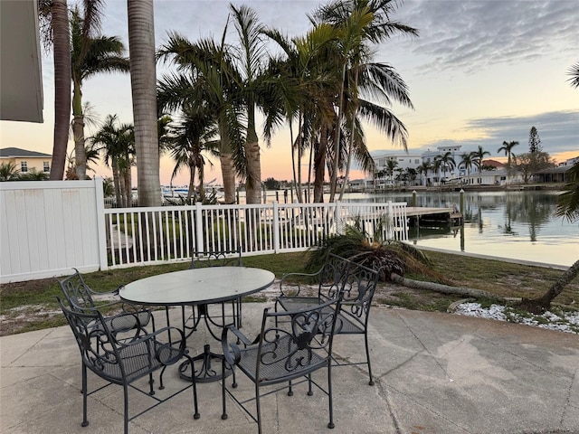 patio terrace at dusk featuring a water view and a boat dock