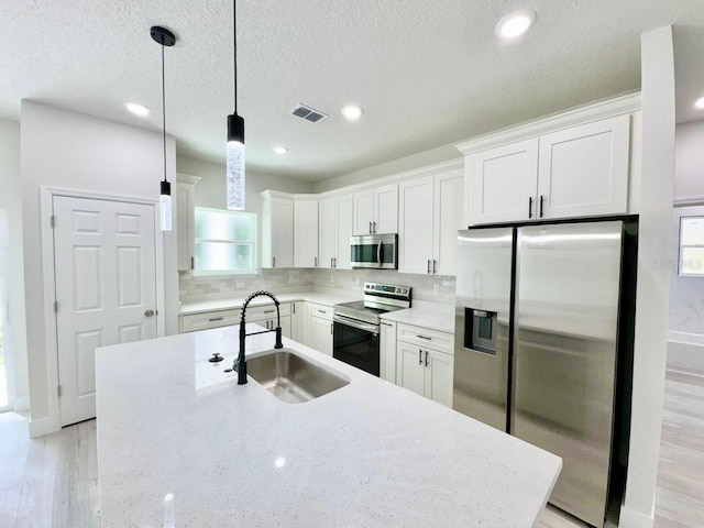 kitchen featuring stainless steel appliances, sink, white cabinetry, decorative backsplash, and hanging light fixtures