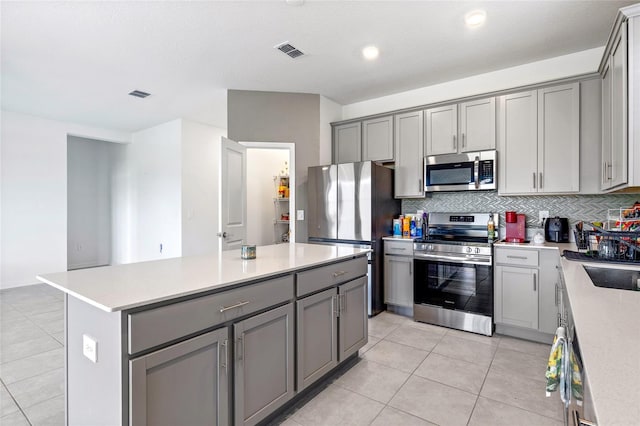 kitchen with tasteful backsplash, gray cabinets, a center island, light tile patterned flooring, and appliances with stainless steel finishes