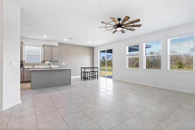 kitchen with a center island, backsplash, light tile patterned flooring, ceiling fan, and gray cabinetry