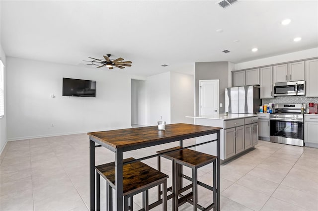 kitchen with appliances with stainless steel finishes, tasteful backsplash, ceiling fan, light tile patterned floors, and gray cabinetry