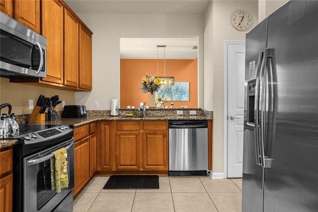 kitchen featuring sink, dark stone countertops, light tile patterned floors, decorative light fixtures, and stainless steel appliances