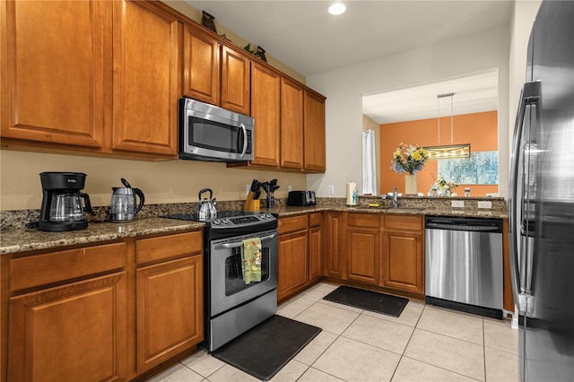 kitchen with sink, dark stone countertops, pendant lighting, light tile patterned flooring, and appliances with stainless steel finishes