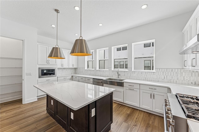 kitchen with light stone countertops, appliances with stainless steel finishes, a kitchen island, white cabinetry, and hanging light fixtures