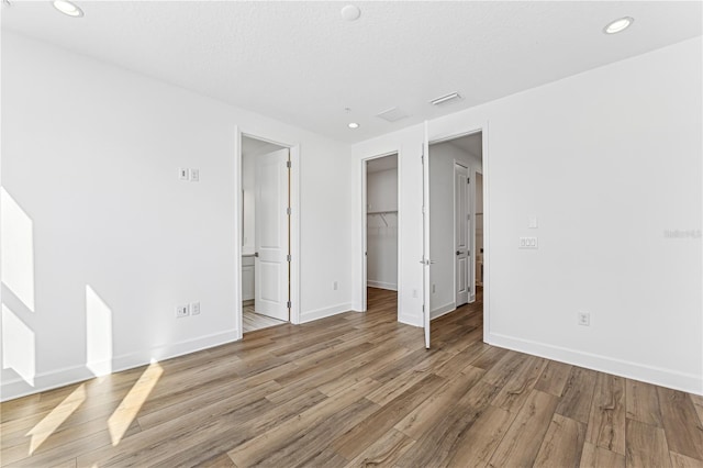 unfurnished bedroom with light wood-type flooring, a closet, a walk in closet, and a textured ceiling