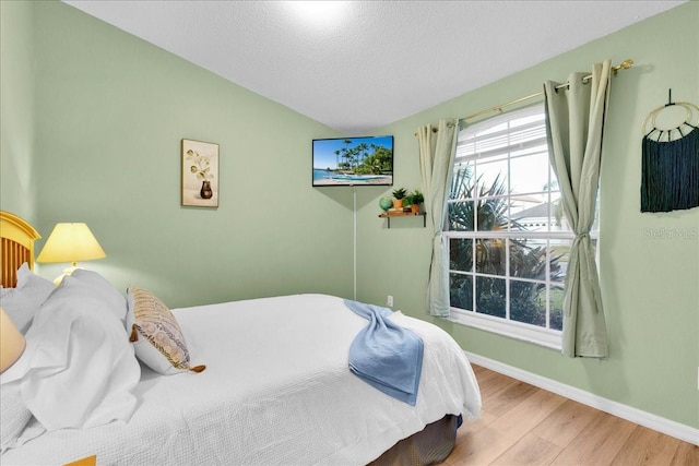 bedroom with lofted ceiling, a textured ceiling, and light hardwood / wood-style floors