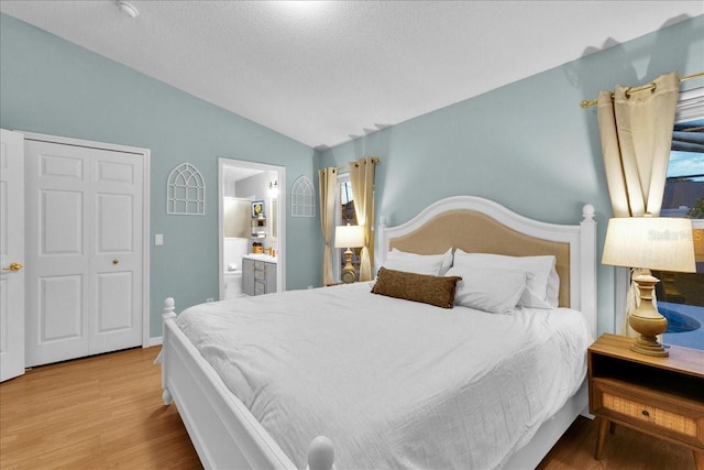 bedroom featuring lofted ceiling, a textured ceiling, light wood-type flooring, and ensuite bath