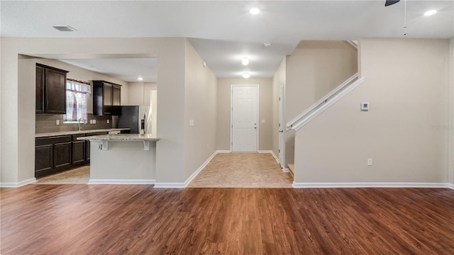 kitchen with stainless steel refrigerator with ice dispenser, hardwood / wood-style floors, light stone counters, and backsplash