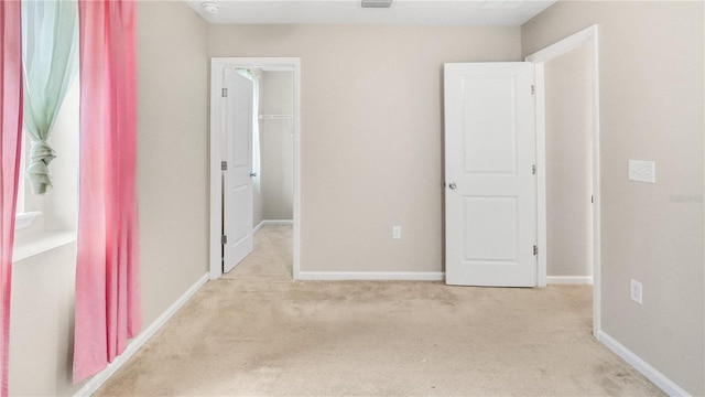 unfurnished bedroom with a closet, a spacious closet, and light carpet