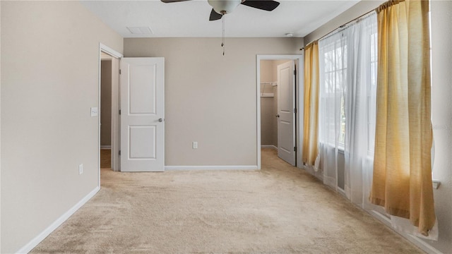 unfurnished bedroom with light carpet, a walk in closet, a closet, and ceiling fan