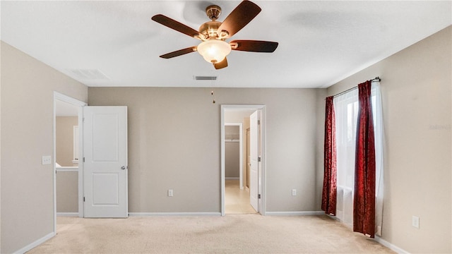 unfurnished bedroom with ceiling fan, light carpet, and a walk in closet