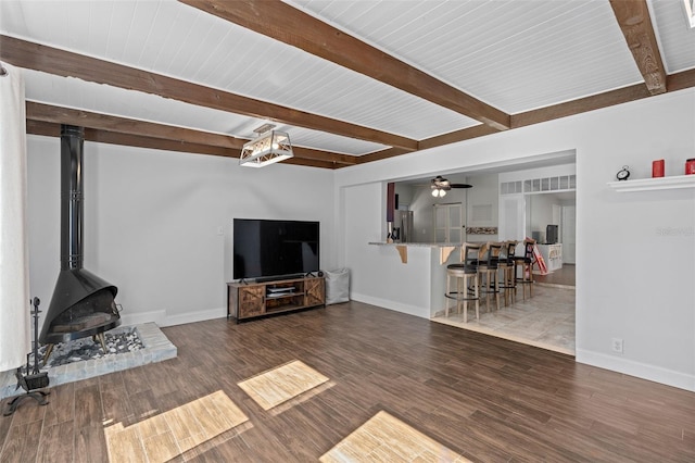 living room featuring ceiling fan, a wood stove, hardwood / wood-style floors, and beam ceiling