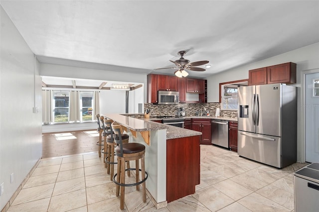 kitchen featuring light tile patterned floors, ceiling fan, stainless steel appliances, backsplash, and a breakfast bar