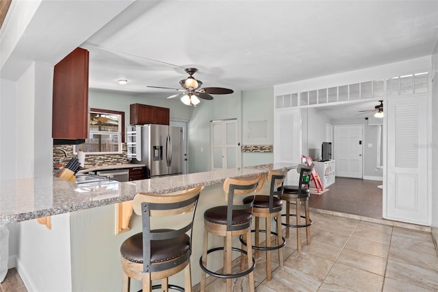 kitchen featuring stainless steel fridge with ice dispenser, kitchen peninsula, a breakfast bar area, and tasteful backsplash