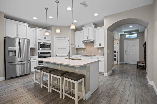 kitchen featuring sink, an island with sink, decorative light fixtures, white cabinets, and appliances with stainless steel finishes