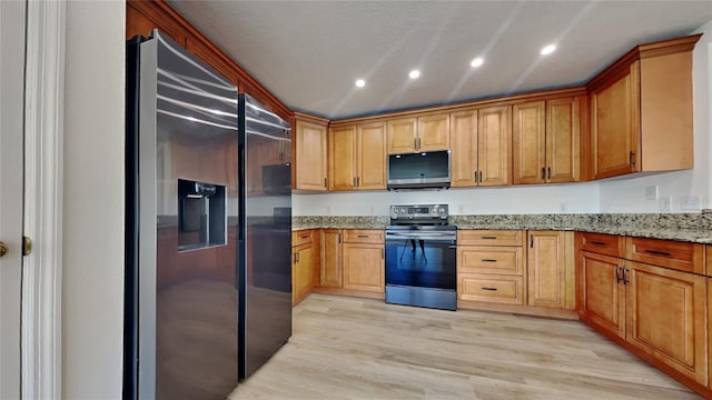 kitchen with light wood-type flooring, stainless steel appliances, and light stone counters