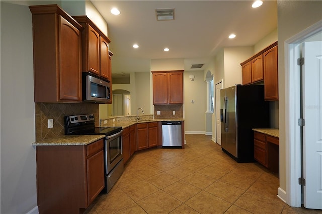 kitchen featuring light stone countertops, appliances with stainless steel finishes, backsplash, sink, and light tile patterned flooring