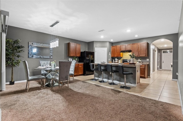 kitchen with black fridge with ice dispenser, a center island, a breakfast bar area, hanging light fixtures, and light colored carpet