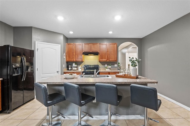 kitchen featuring black appliances, an island with sink, a kitchen bar, and light tile patterned floors